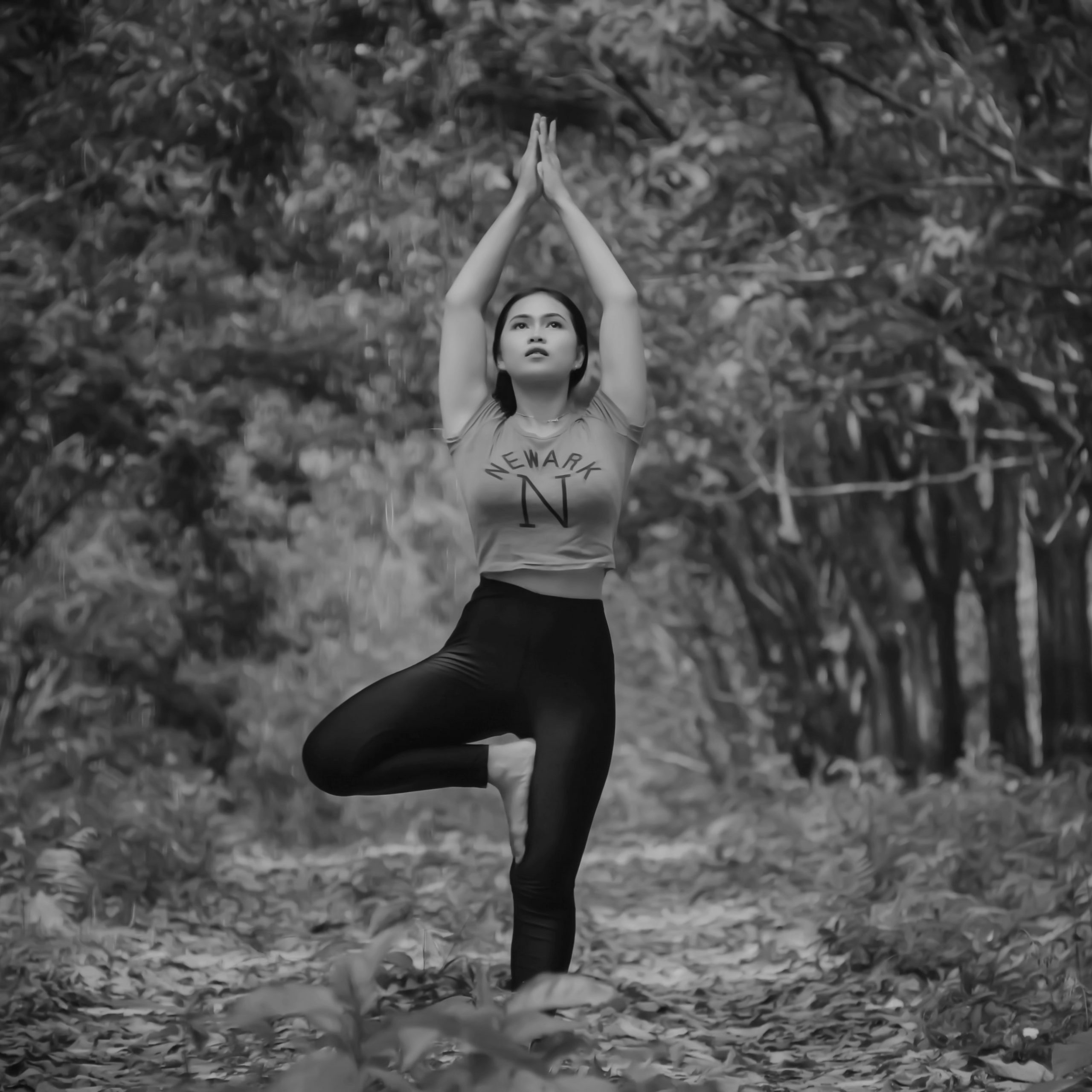 Lady doing light workout by standing on one leg and having her arms above head in the nature